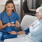 Female nurse checking blood pressure of senior woman at home